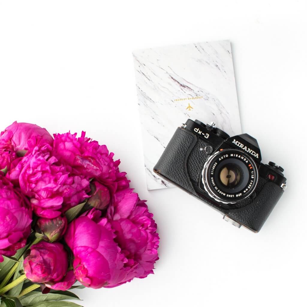 Camera on a desk with pink flowers and a notebook