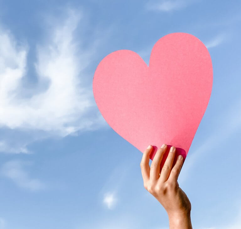 A pink cardboard heart held up against a blue sky backdrop